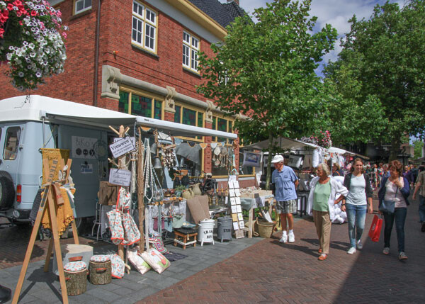 Bezoekers van midzomermarkt wandelen langs marktkramen op de kanaalstraat in Lisse